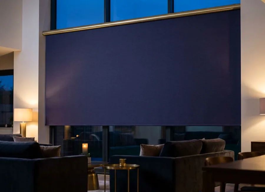 Blockout roller blind lowered over double-height windows at dusk
